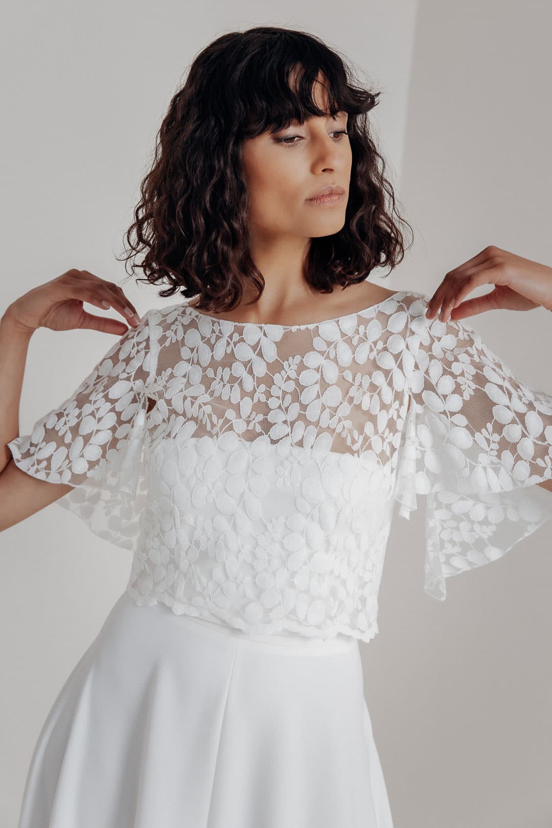 Lucy is een elegante bruidstop die overtuigt door verfijnde details:

vloeiende, wijde vleermuismouwen zorgen voor een levendige, luchtige look en een comfortabele pasvorm. De tijdloze boothals die aan de achterkant uitloopt in een V, een kleine knoopsluiting onderaan de achterkant en een romantisch geschulpt randje maken van de kanten top Lucy het key piece van jouw bruidslook.

Met zijn patroon gemaakt van de populaire bladkant, verwijst het naar enkele van de favoriete tops uit eerdere noni-trouwjurkcollecties. Het tijdloos mooie patroon komt door de romantische volantsmouwen bijzonder mooi tot zijn recht. 