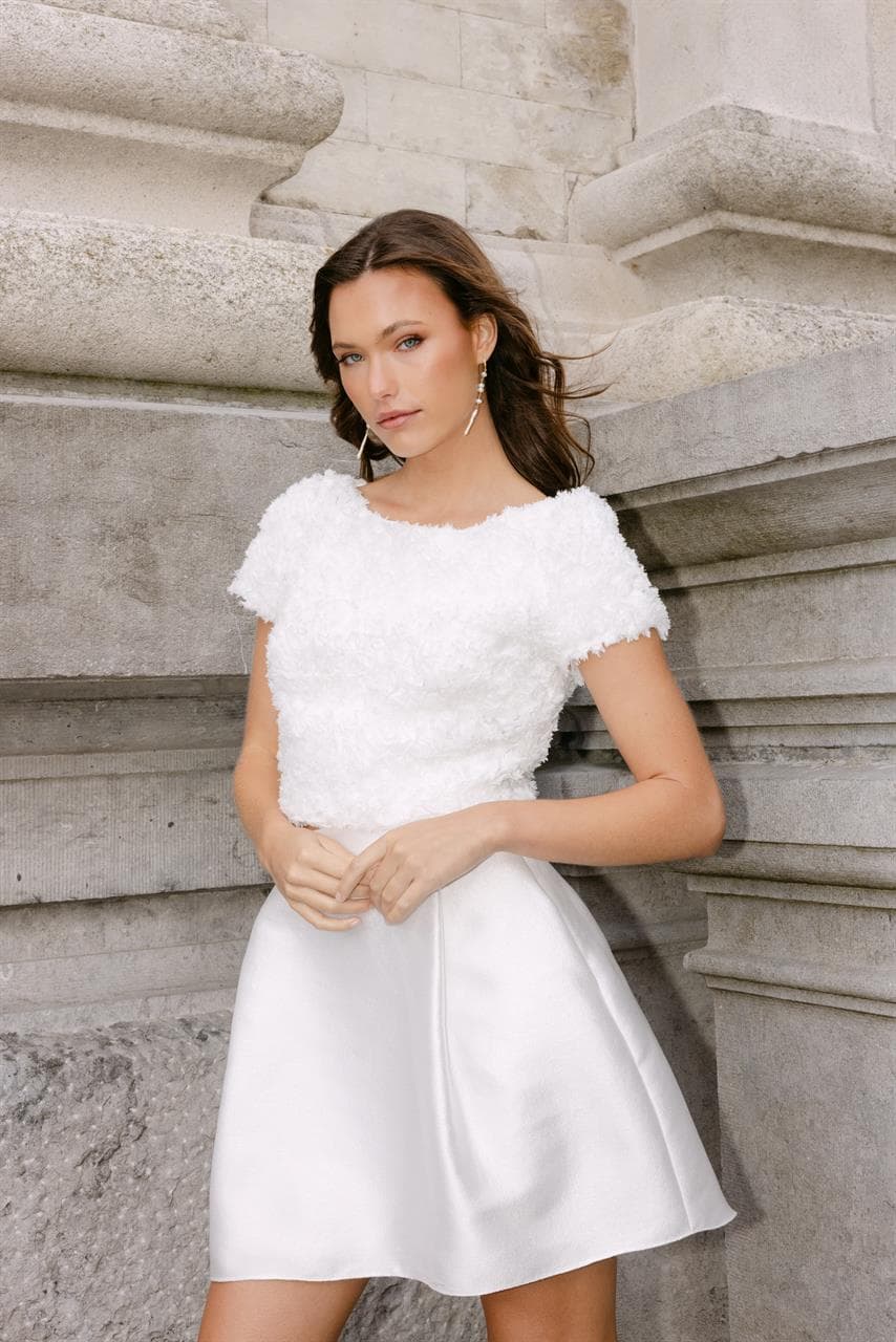 Luna is een tweedelige set die bruidselegantie een nieuwe definitie geeft met een eigentijdse twist. De getailleerde top met korte mouwen is gemaakt van een structuurstof, subtiel versierd met delicate bloemen. Gecombineerd met een strakke, wikkelrok van glanzend satijn, waar discrete zakken een vleugje functionaliteit toevoegen.